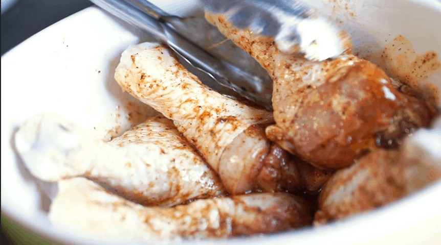 uncooked chicken legs being tossed in paprika seasoning