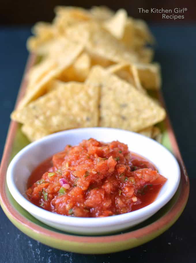 white bowl of salsa on platter with tortilla chips on blue background