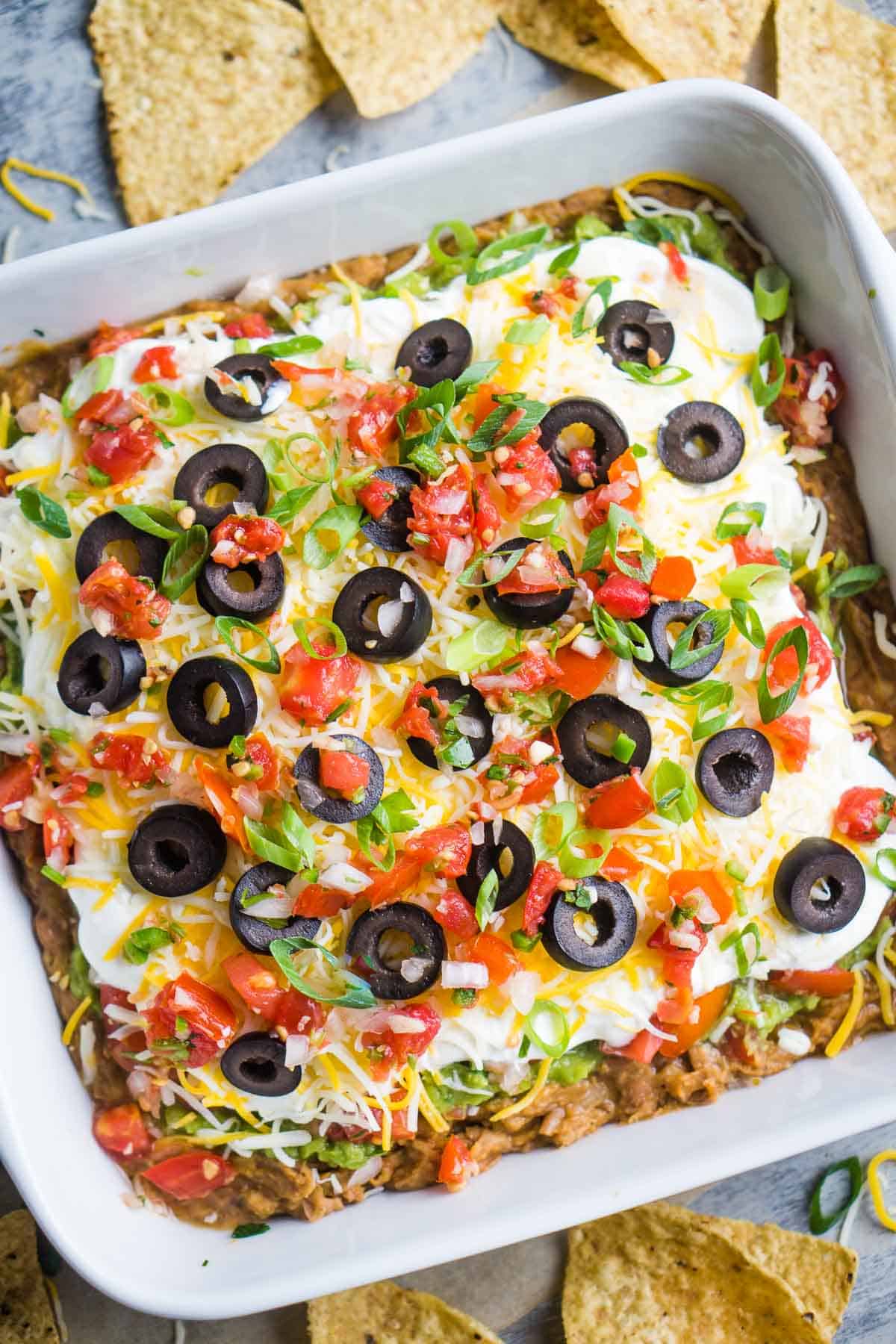 seven layer dip in square white dish with scattered tortilla chips