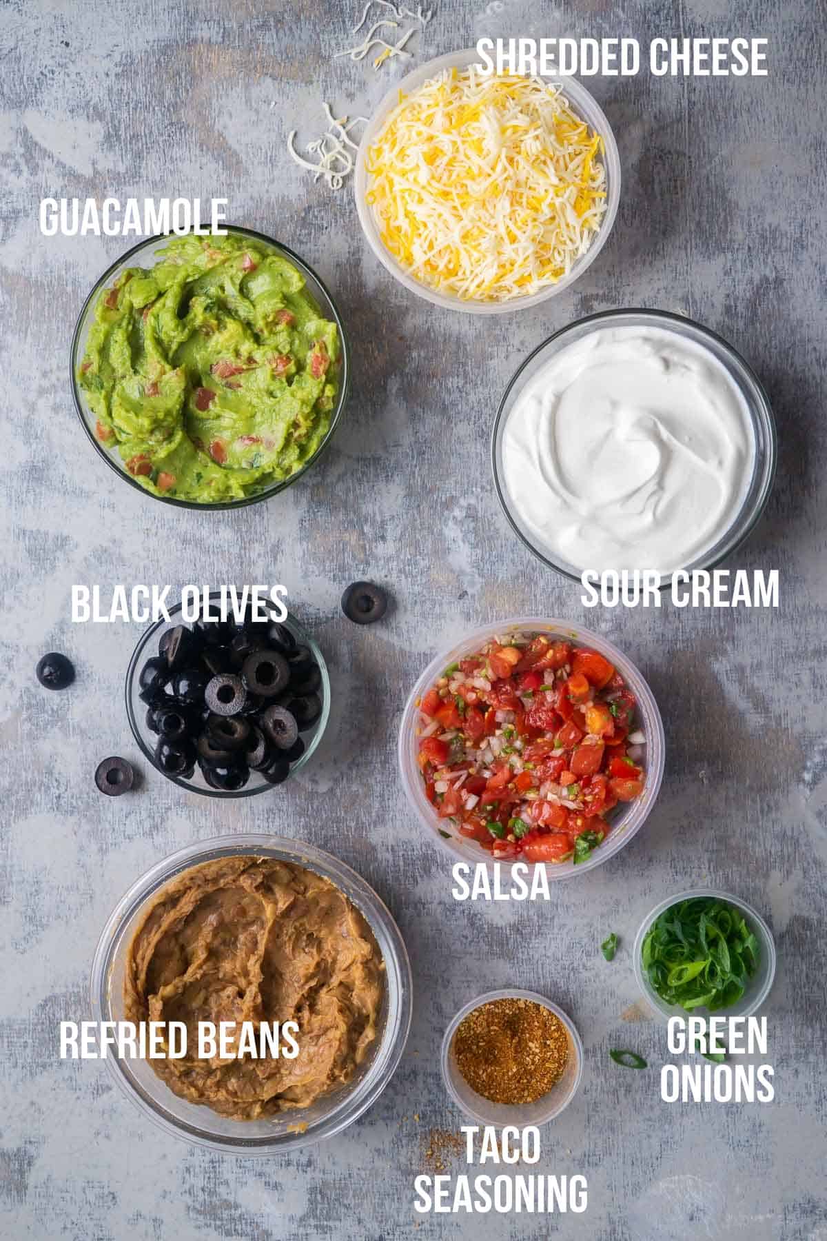 seven layer dip ingredients in separate bowls labeled