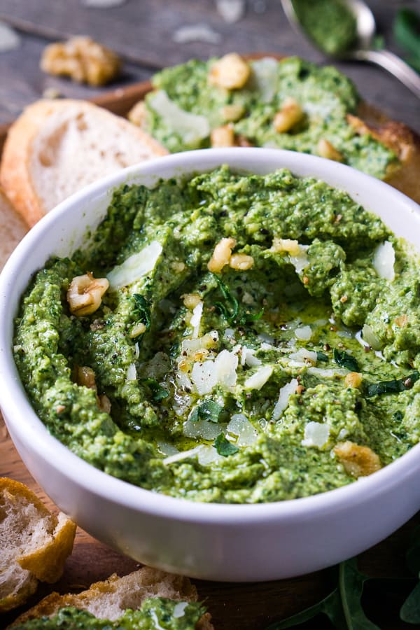 arugula pesto in white bowl on wooden platter with bread