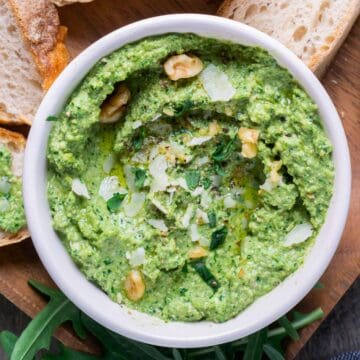 arugula pesto in white bowl on brown wood serving platter with sliced french bread