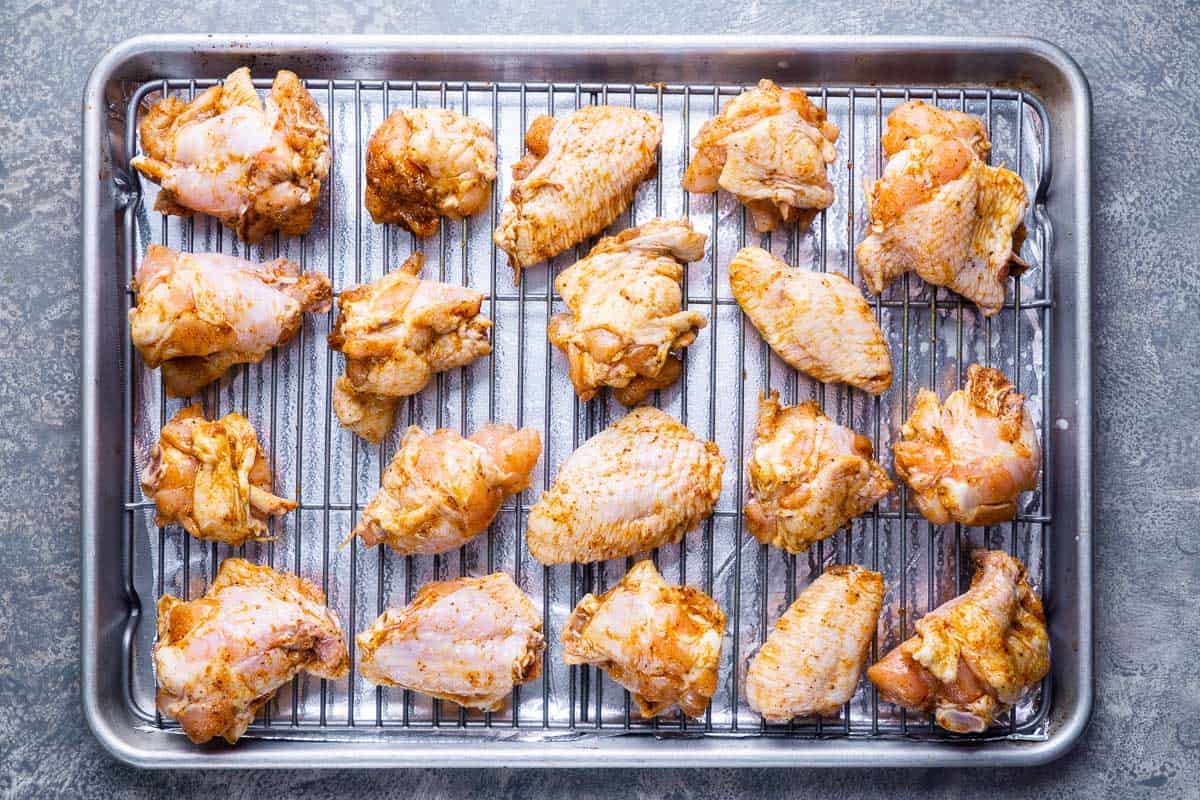 uncooked seasoned chicken wings on baking sheet with baking grid