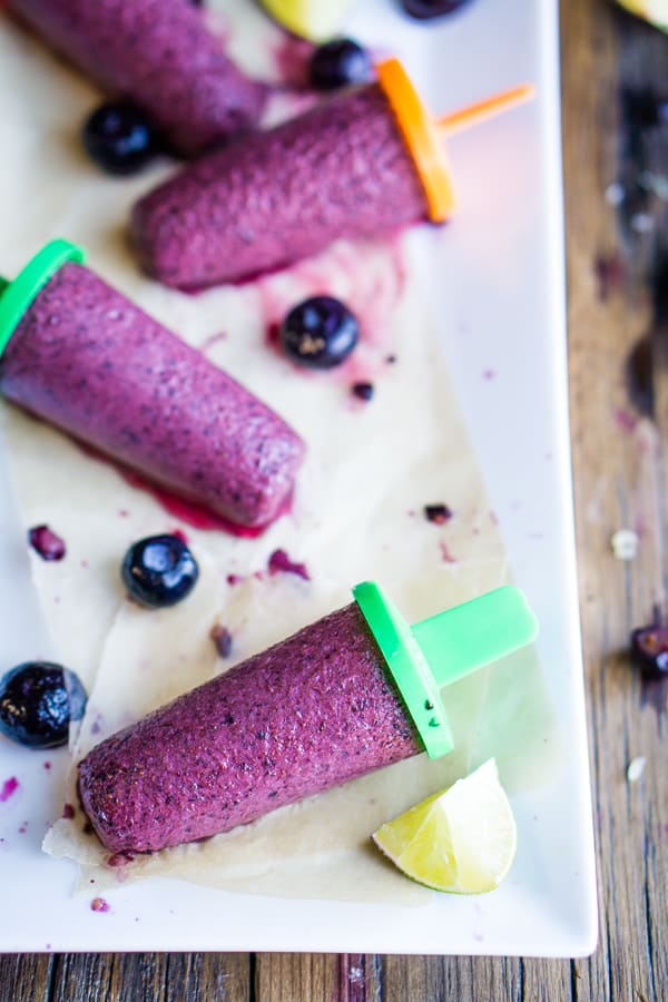 blueberry popsicles on parchment paper on white plate with blueberry and lemon garnish