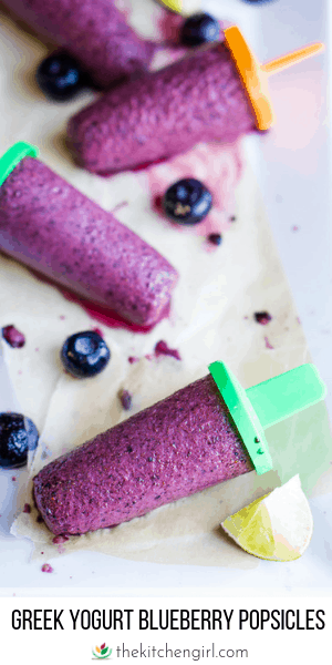 blueberry popsicles on parchment paper on white plate with blueberry and lemon garnish