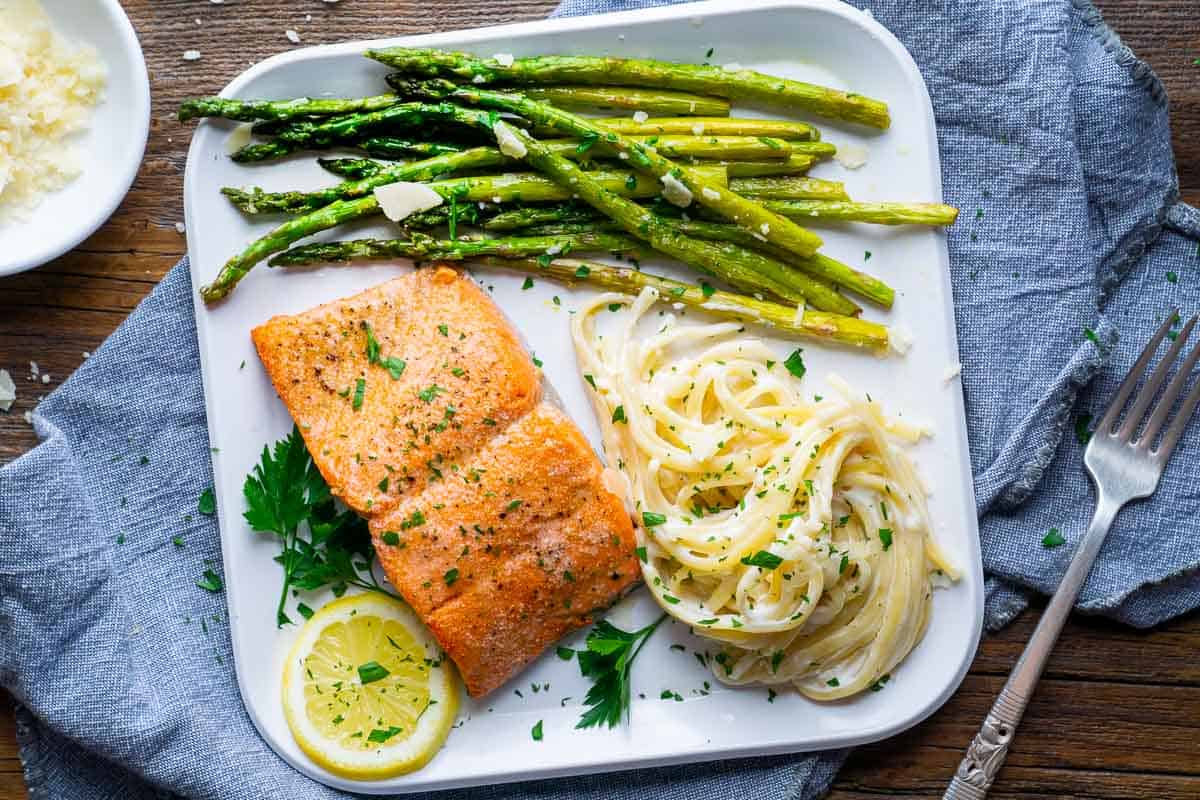 broiled salmon fillet next to asparagus and pasta noodles on white plate