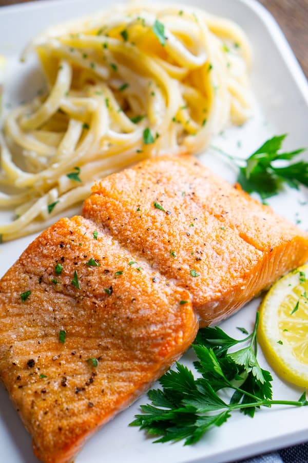 broiled salmon and fettuccini alfredo on white plate with lemon and parsley garnish
