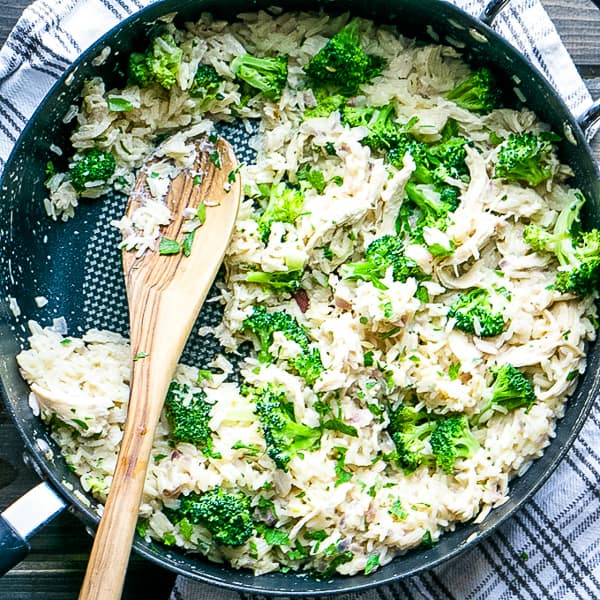 skillet of chicken broccoli rice on white and gray towel with lemon and parsley on gray wood backdrop