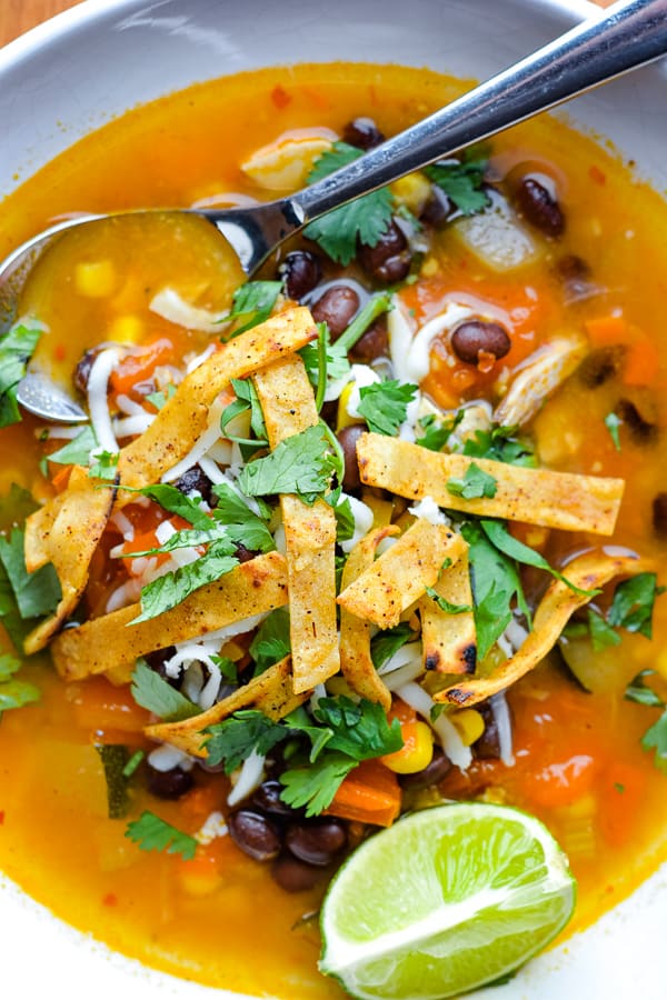 chicken tortilla soup in white bowl with spoon garnished with lime