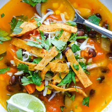 chicken tortilla soup in white bowl with spoon garnished with lime