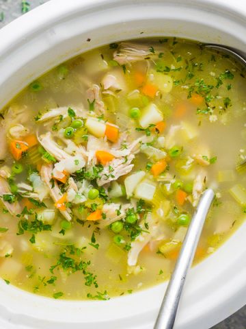chicken vegetable soup in white crockpot slow cooker with soup ladle