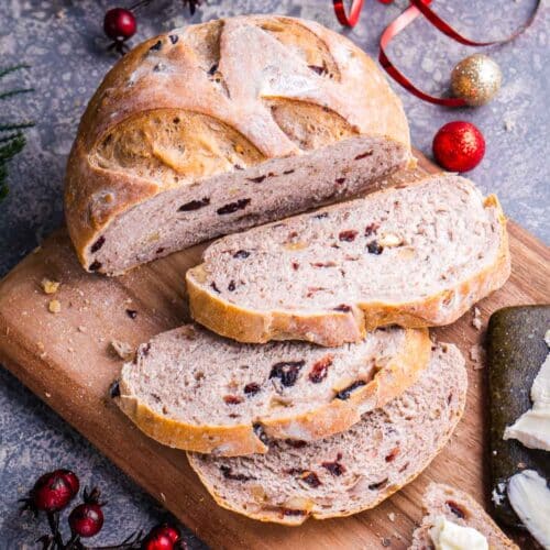 plump loaf of sliced cranberry walnut bread on cutting board next to holiday decorations