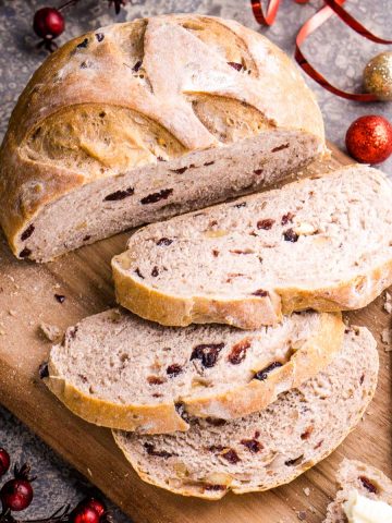 sliced cranberry walnut bread loaf on cutting board next to Christmas decorations