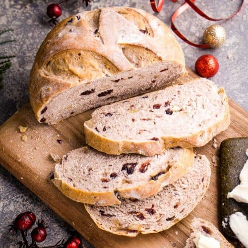 sliced cranberry walnut bread loaf on cutting board next to Christmas decorations