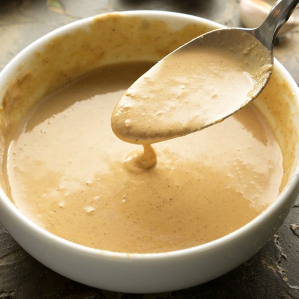 Spoonful of Thai peanut sauce over white bowl
