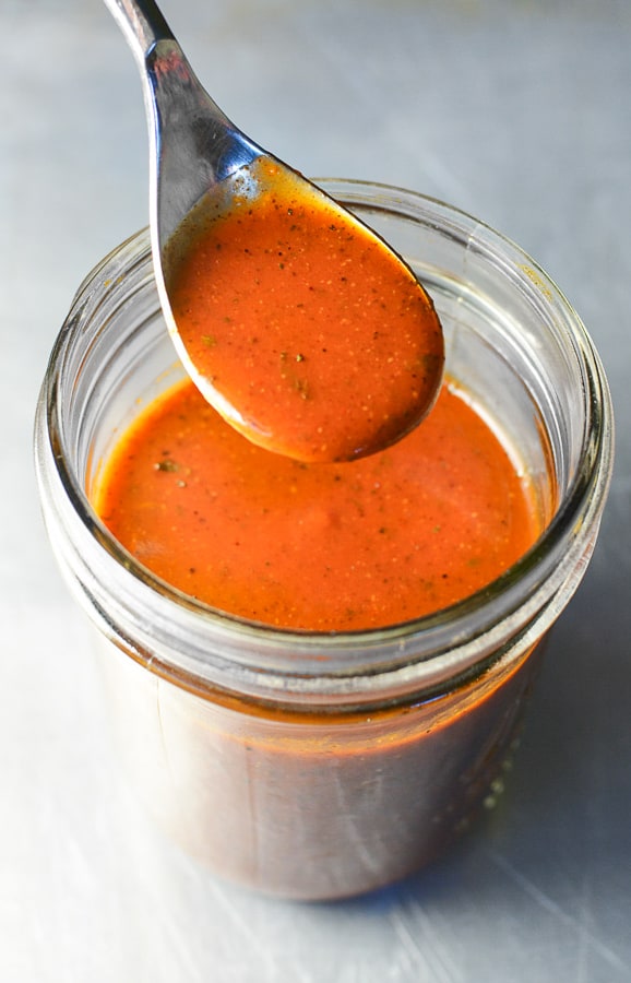 glass jar of red enchilada sauce with a spoon portion