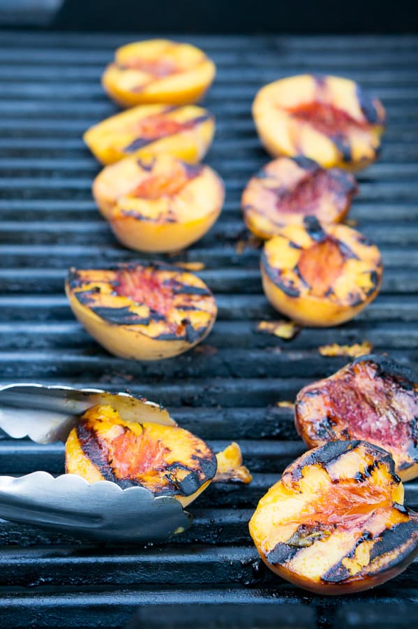 Peach halves being turned on a hot grill