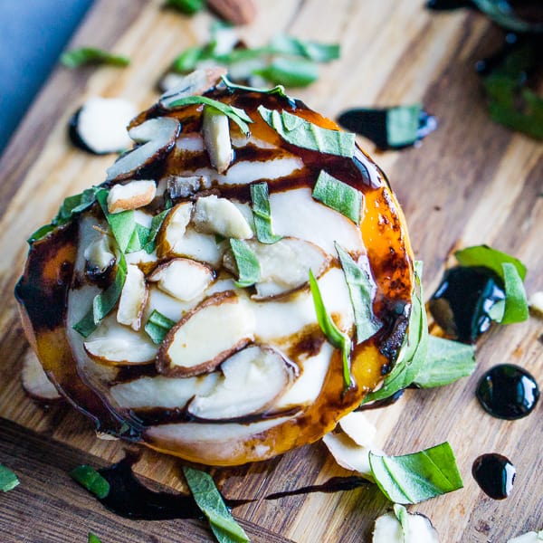 Grilled peaches filled with mozzarella cheese, almonds, basil, and balsamic drizzle served on a brown cutting board