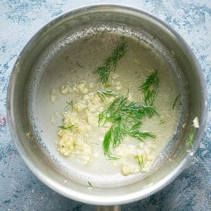 garlic dill butter in stainless sauce pot on blue gray background