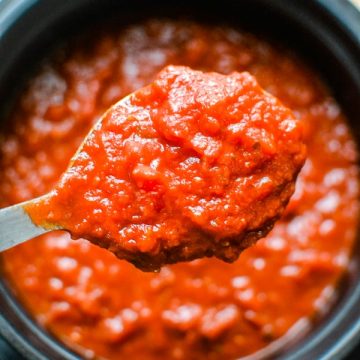 close up of red homemade tomato sauce on serving spoon over pot of sauce