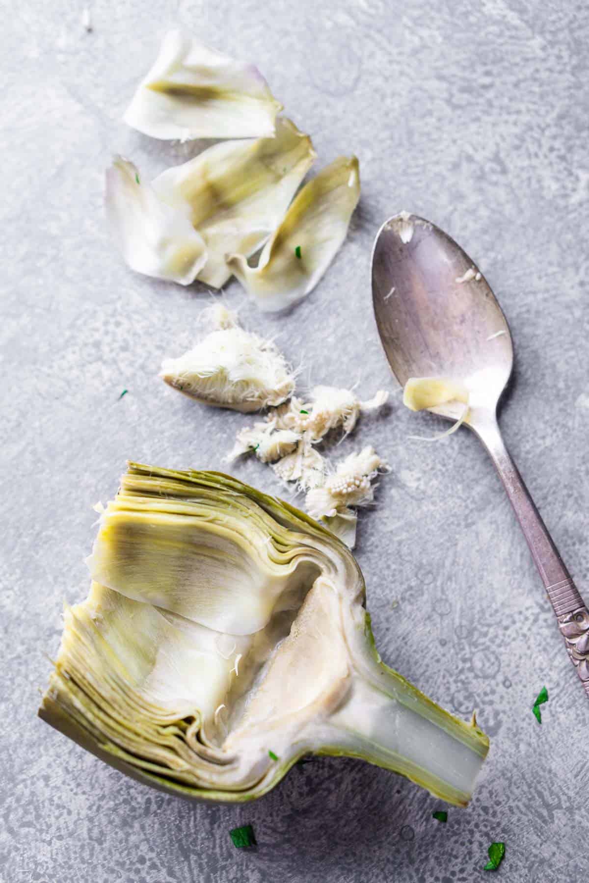cooked artichoke half with choke removed next to spoon