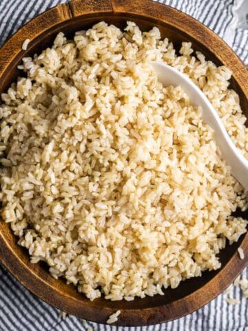fluffy cooked brown rice in wood serving bowl with white rice paddle
