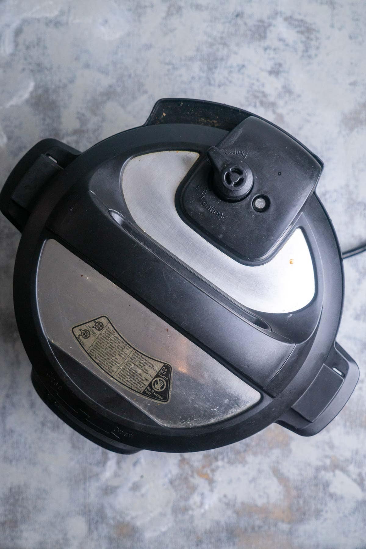 A top-down view of a closed Instant Pot with a black and silver lid placed on a textured gray surface.