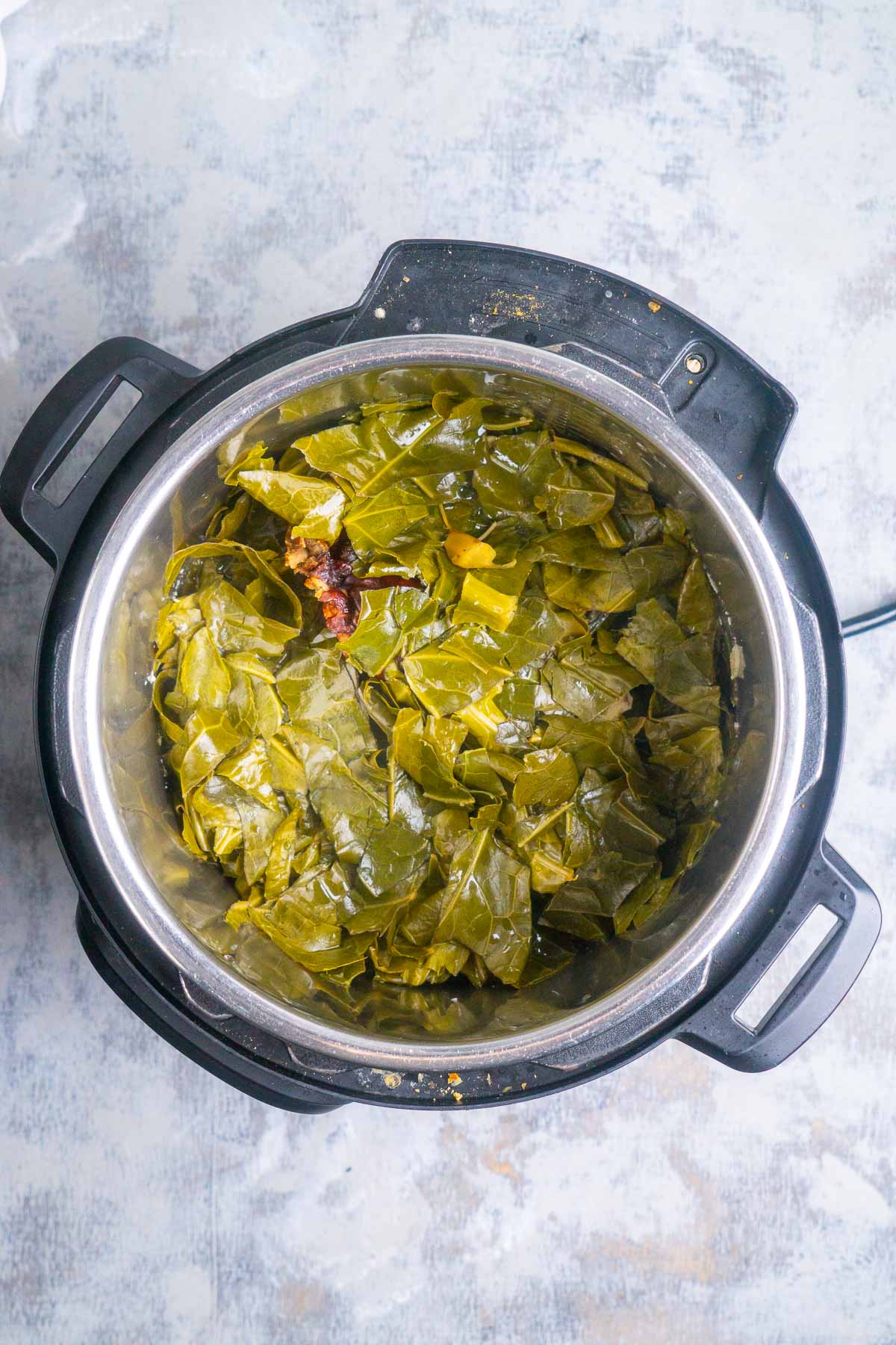 Tender collard greens cooked in an Instant Pot, viewed from above, with a piece of smoked meat nestled among the flavorful greens.