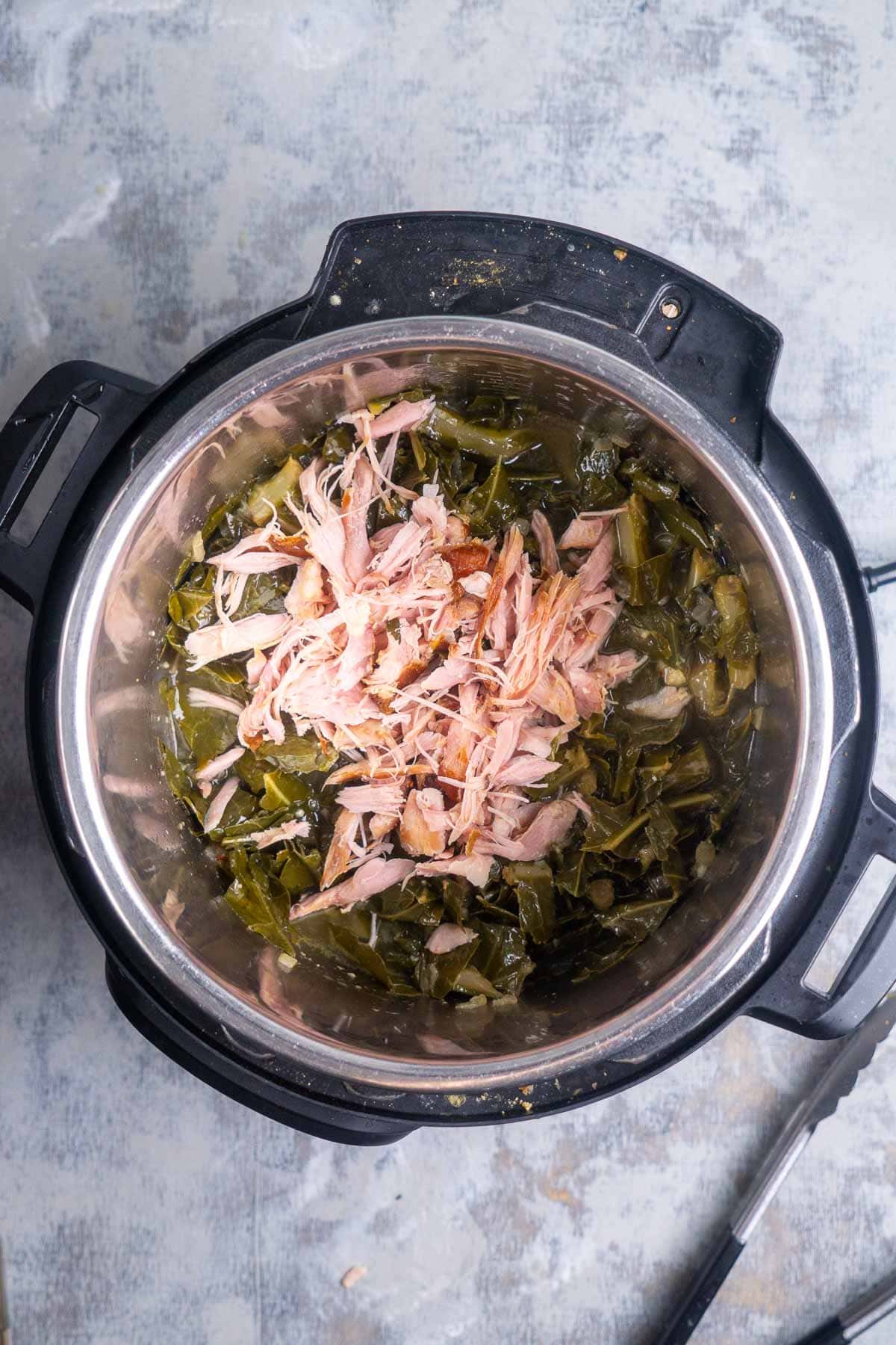 Shredded turkey and collard greens inside an open Instant Pot on a gray surface.