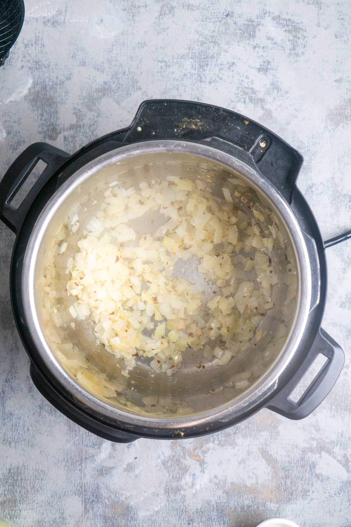 Chopped onions saut&eacute;ing in an open pressure cooker, seen from above on a light-colored surface.