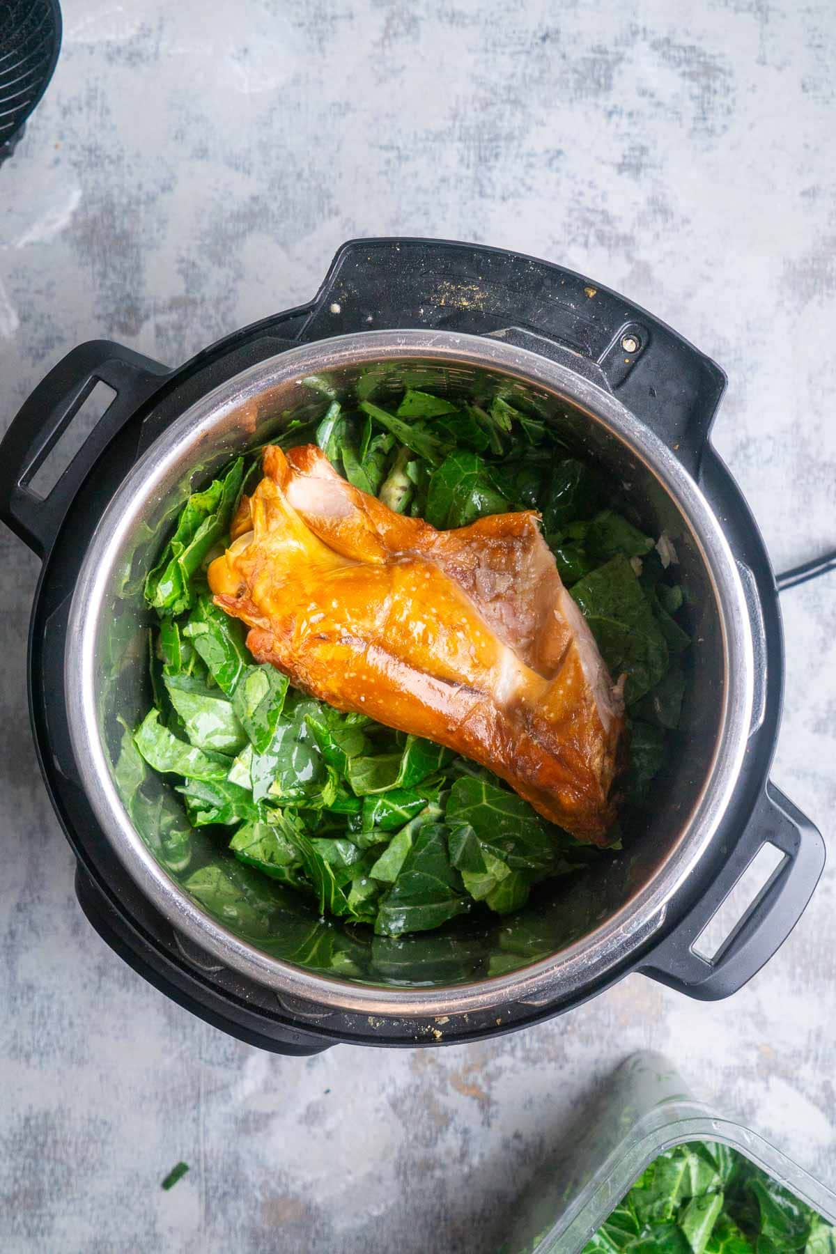 An overhead view of an Instant Pot containing chopped collard greens and a large smoked turkey wing, ready to be pressure cooked.