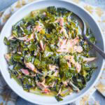 A bowl of savory collard greens mixed with shredded turkey, served in a flavorful broth with a spoon.