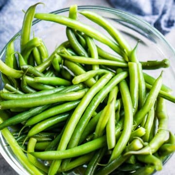 green beans in glass bowl next to tongs and blue linen