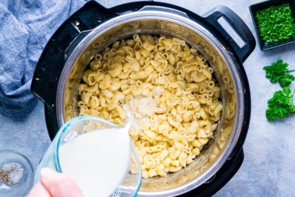 top down view of hand pouring milk into Instant Pot with mac and cheese ingredients