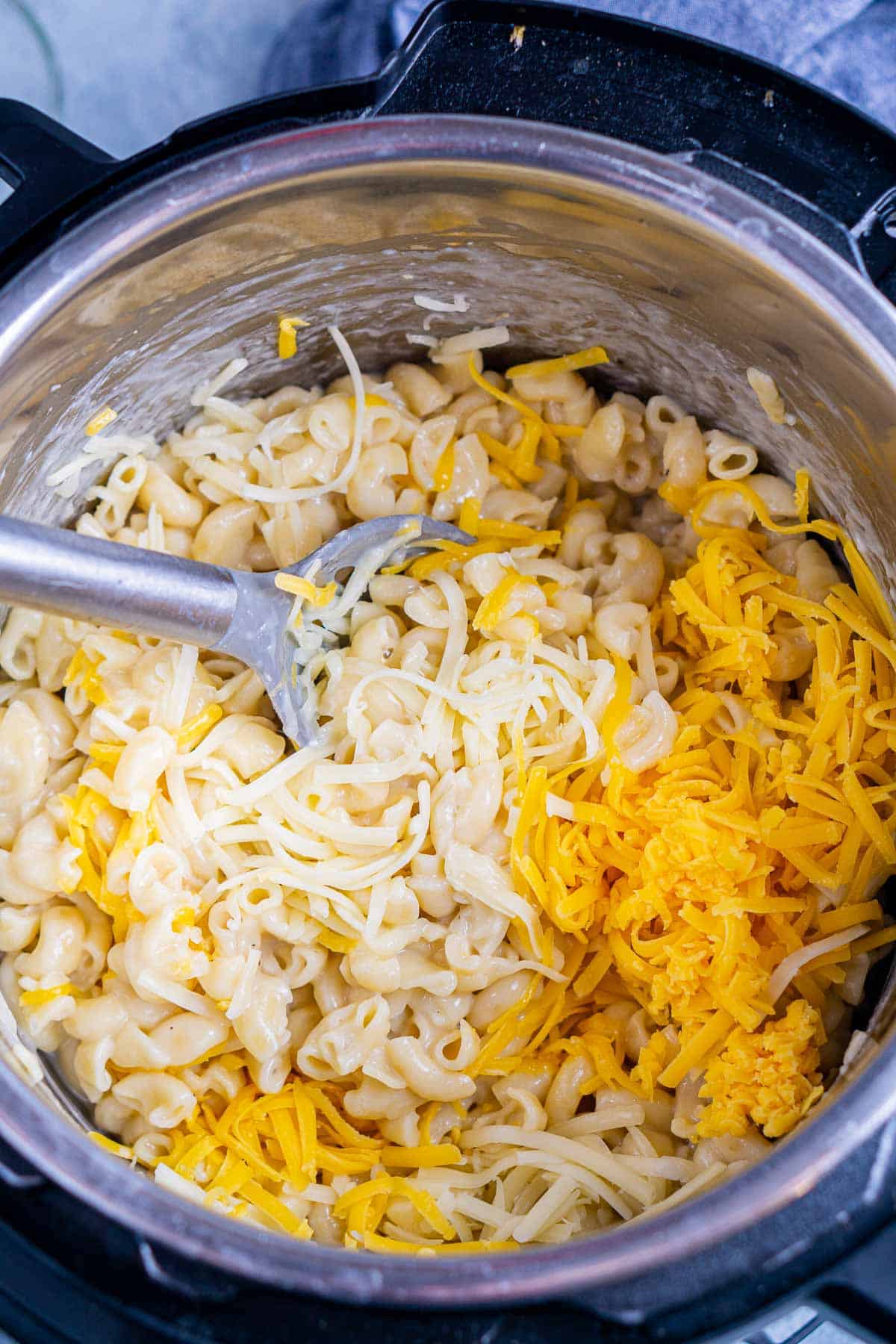spoon stirs shredded cheese into macaroni noodles in Instant Pot