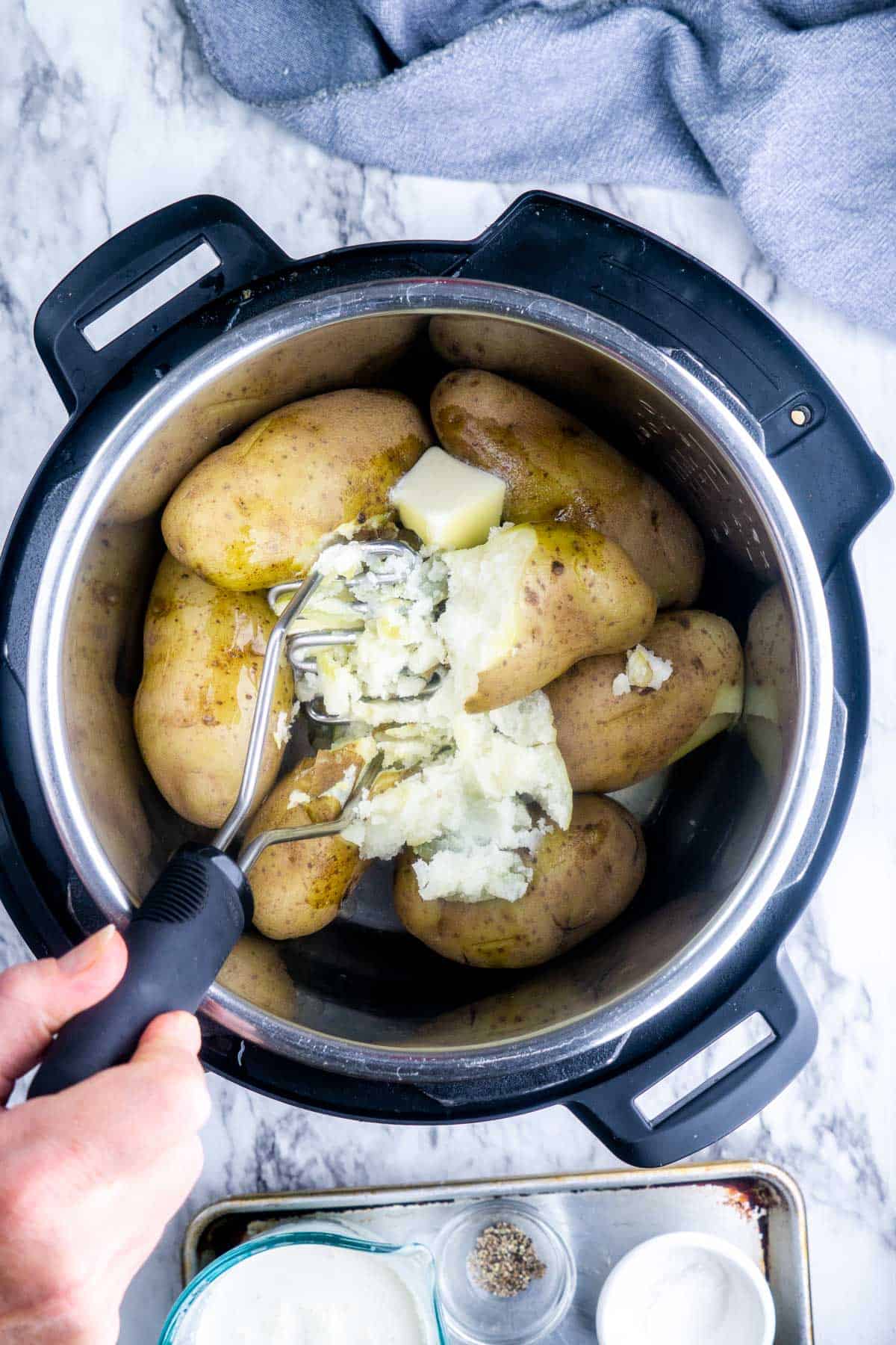 whole cooked potatoes in Instant Pot are being mashed by potato masher