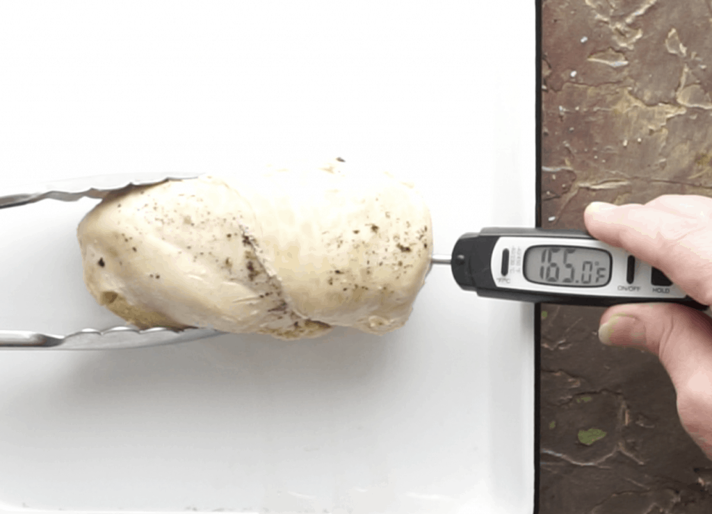 Meat thermometer inserted in cooked chicken breast registering 165°F