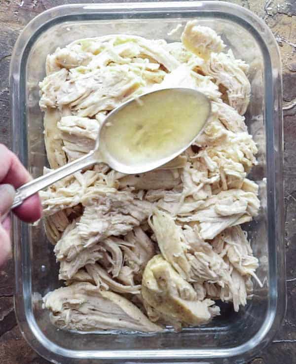 Spooning juice over pulled chicken breast in glass meal prep container