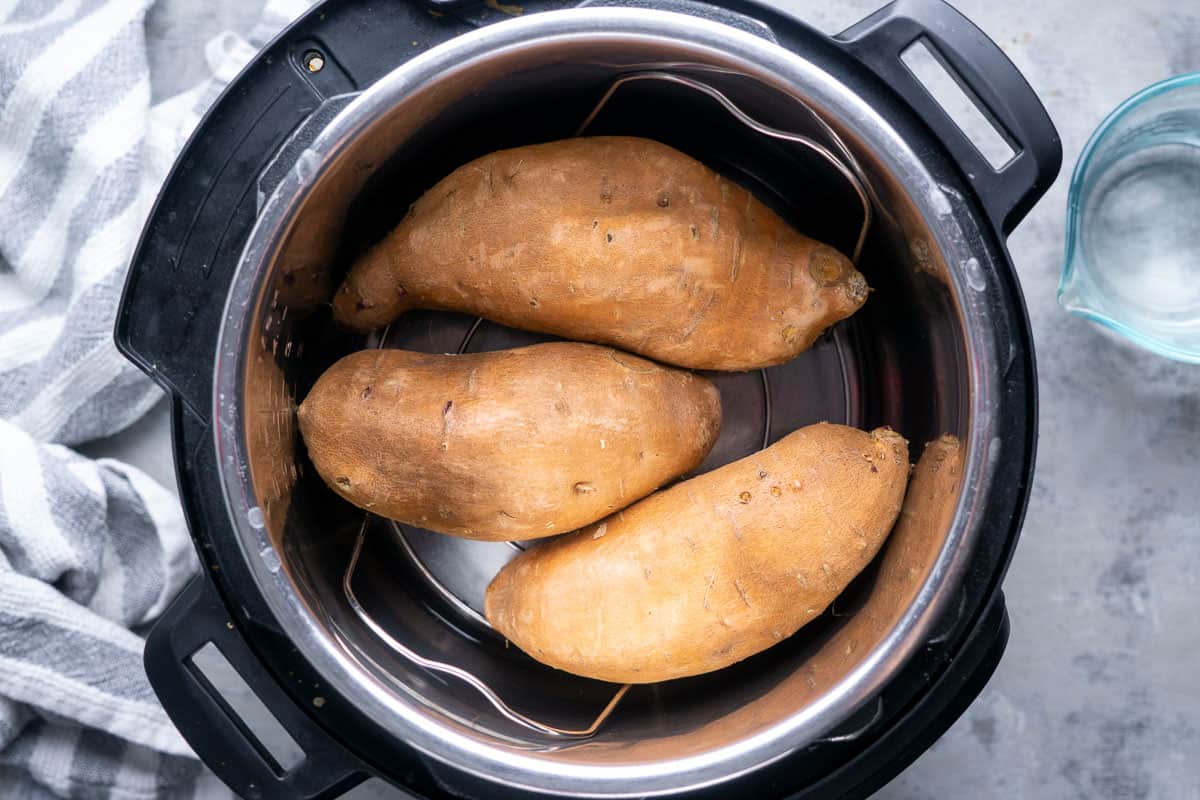Three uncooked sweet potatoes on a trivet in the instant pot
