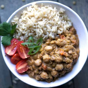 lentil chickpea curry, rice, tomatoes, and cilantro in white bowl on blue background