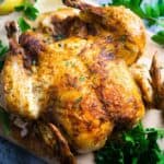 whole chicken on serving board with parsley and lemon garnish