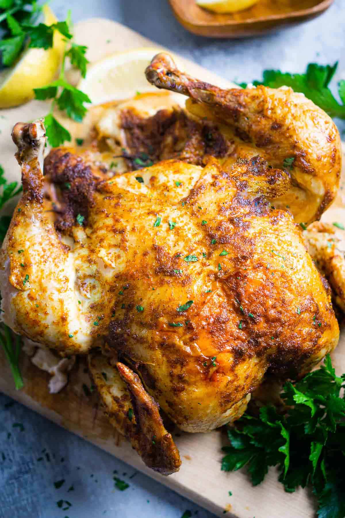 whole chicken on serving board with parsley and lemon garnish