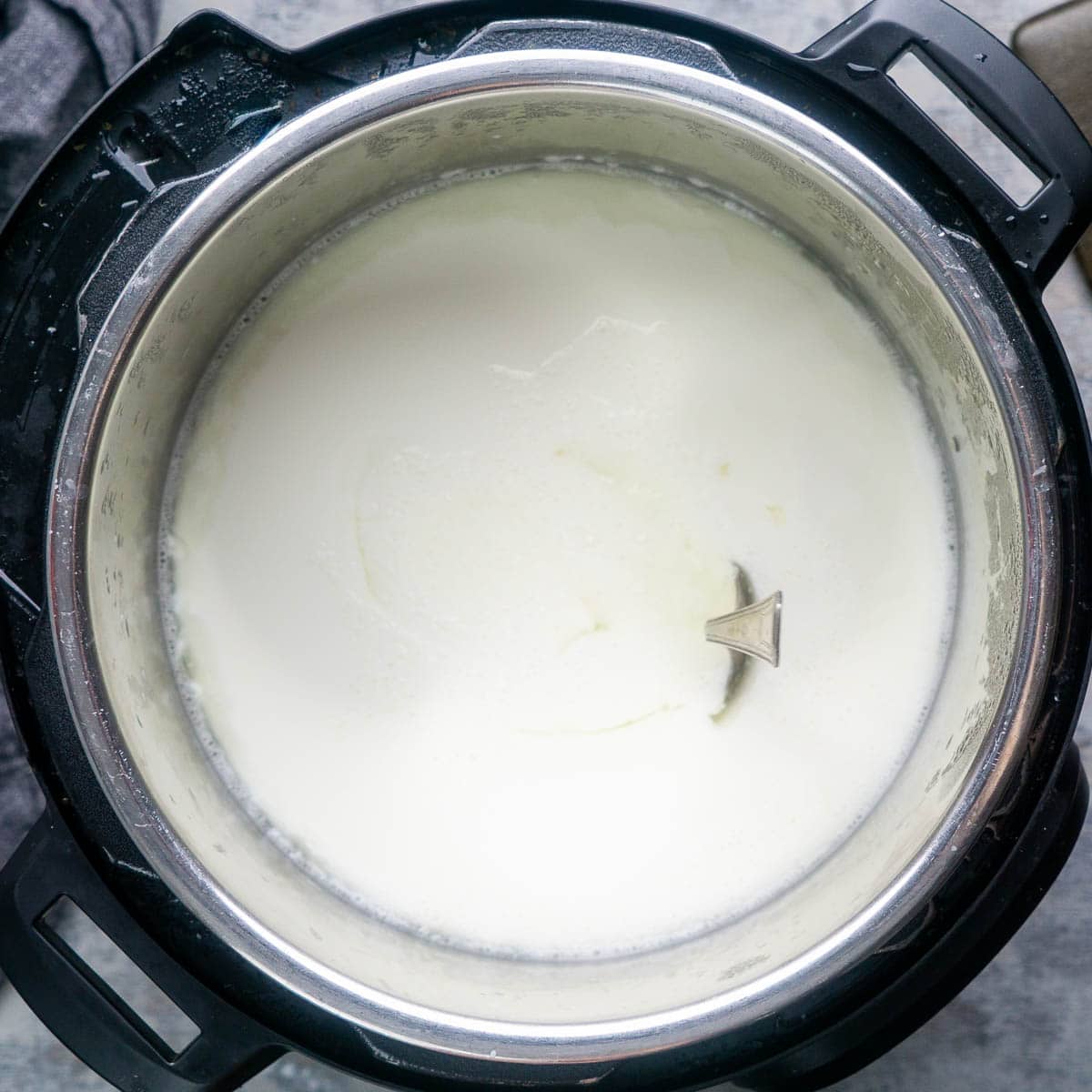 A spoon stands upright in yogurt in the Instant Pot to confirm the yogurt has fully set up.
