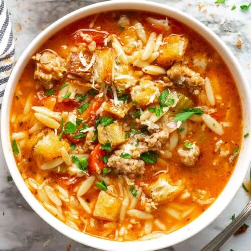 Italian sausage soup in white bowl garnished with croutons and parsley