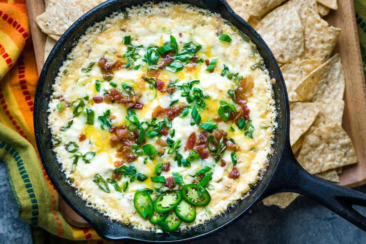 baked jalapeno popper dip in iron skillet next to tortilla chips and colorful napkin