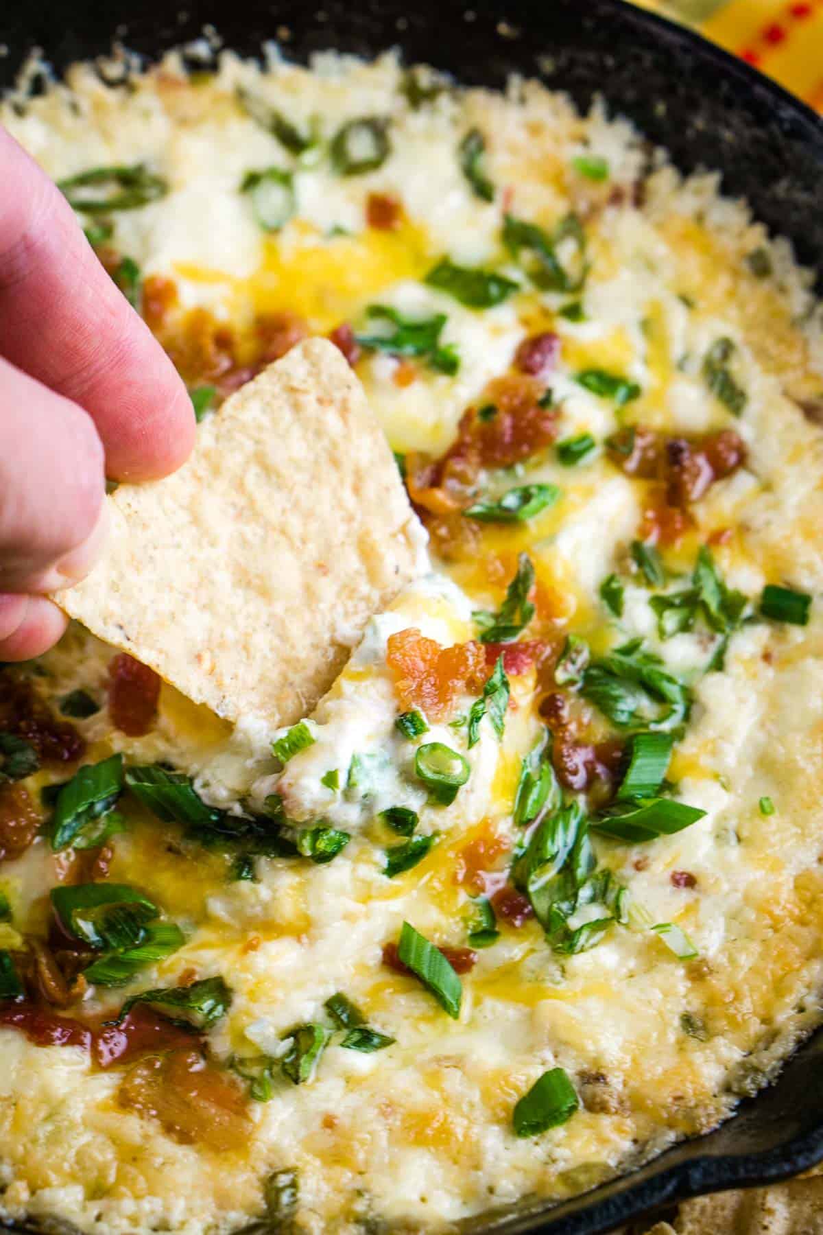 Hand is scooping up jalapeno popper dip with a tortilla chip