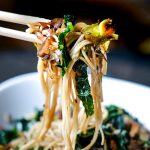 chopsticks with kale sesame noodles over white bowl