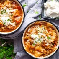 lasagna soup in ceramic cups on blue linen with ricotta cheese and parsley garnish