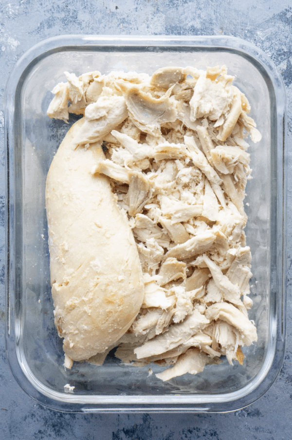 shredded chicken breast or turkey breast in glass meal prep container on grey background
