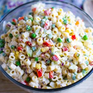 Macaroni salad in glass bowl on beige table with colorful linen and wooden spoon